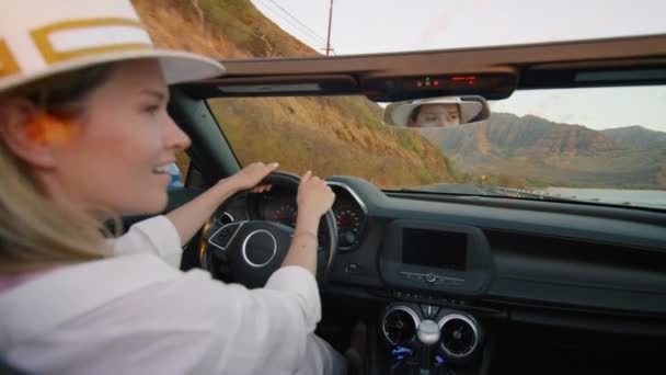 コンバーチブルカーの後部座席からの眺め 夏休みにカブリオレの車を運転するスタイリッシュな白い服の女性 映画の火山山でオアフ島を探索する幸せな旅行者 ガールを感じる無料 — ストック動画