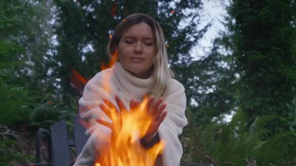 一个微笑的女人在篝火中取暖的画像 快乐的女性享受着周末外出时焚烧篝火的自然之旅 在绿云杉森林背景的火坑外的令人满意的游客 — 图库视频影像