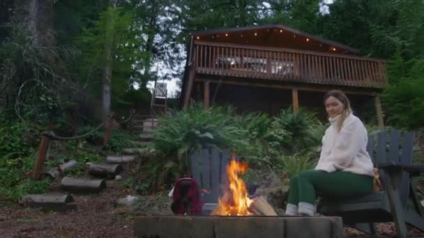 在绿林失火时 女性在村舍室外放松的低角度镜头 周末出游 自然目的地 在木屋外面的火坑里烧木柴的年轻女人 — 图库视频影像