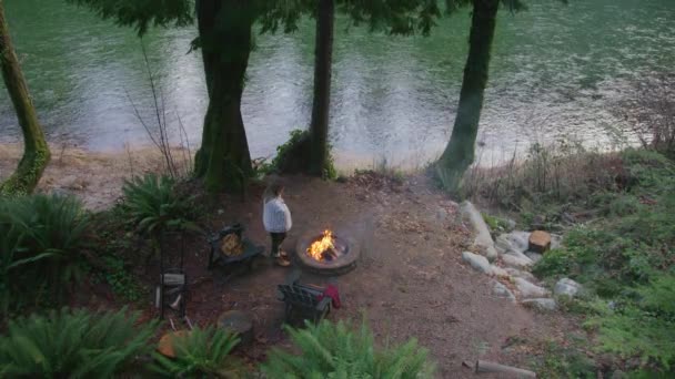 週末の休暇中に火のピットで暖まる居心地の良い毛布で包まれた女性の頭上ビュー 緑の川で燃える火を楽しむリラックスした女性 背景に緑のスプルースの森で燃えている女性 — ストック動画