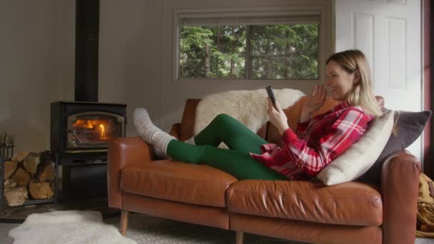 女人们在森林小木屋里用移动相机 在烧木柴的火炉边取暖 偏远目的地的人员和技术 年轻女子在舒适的沙发上用手机拍照 — 图库视频影像