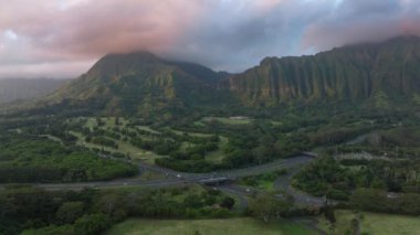 Otobandan geçen arabalar volkanik dağ sırtı boyunca sinematik bulutlarla kaplıdır. Yeşil dağlarda otoyolda etkileyici bir gündoğumu. Manzaralı doğa Hawaii adası. Destansı Oahu doğası ABD