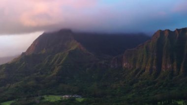 Gün doğumunda sinematik pembe yağmur bulutlarıyla kaplı nefes kesici volkanik dağ sırtı. Hawaii adasının manzaralı doğa manzarası. Dikenli yeşil uçurumları olan destansı Oahu doğası etkileyici gündoğumu 4K