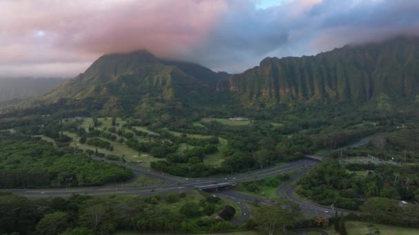 印象的な日の出に緑の山でハイウェイを見る 映画の雲で覆われた火山の尾根に沿って高速道路で運転する車 風光明媚な自然景観ハワイ島 エピックオアフ自然 アメリカ — ストック動画