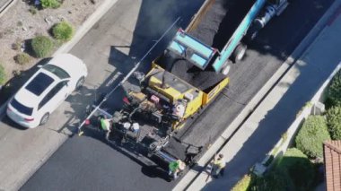 Los Angeles, Kaliforniya, ABD, yeniden yüzeye çıkış süreci Mart 4, 2024: Hava görüntüsü asfalt, büyük patika makinesi ve banliyö bölgesinde güvenlik yelekleri ile asfalt döşeyen bir yol ekibi yakalıyor. 4K. 