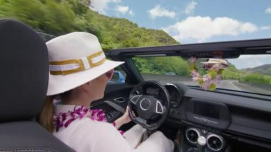 Yeşil dağ manzaralı Oahu adasını keşfeden mutlu bir kadın. Orkide çiçekli gezgin ve beyaz şapkalı çatısız araba süren rüzgarın ve yaz tatilinin güneşli gününün tadını çıkaran.