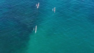 Kanoda yüzen insanların yukarıdan çekimleri. Atletizm takımlarındaki hava manzarası geleneksel Hawaii kanosunun kayığıyla yarışıyor. Koyu mavi okyanus sularında manzaralı su aktivitesi 4K