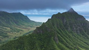 Havai 'de bulutlu bir günde Kualoa vadisi. Manzaralı, tropikal doğa manzarası. Dron yağmurlu dağ sırtı üzerinde uçuyor. Oahu adasında açık hava macerası. Yeşil orman zirvesinin dramatik manzarası