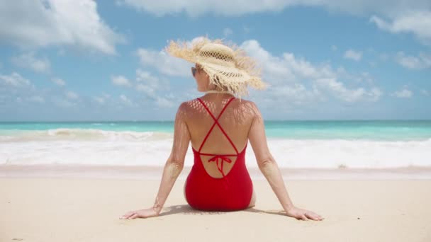 赤い水着とわら帽子のバックビュー女性は海を楽しんでいます シネマティックビーチバケーション4K 人々は夏に美しいティールブルーの海とパラダイス島に旅行します 観光コンセプトのスローモーション — ストック動画