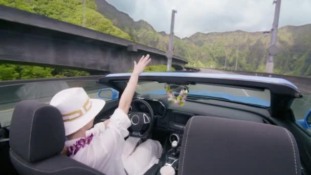 乘坐着蓝色敞篷车在H3高速公路上快乐的游客 从出租汽车上看到的夏威夷风景 莱茵花丛中优雅的女人放弃了车外的手 妇女途经瓦胡岛4K — 图库视频影像