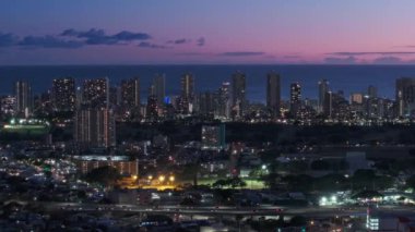 Günbatımında Waikiki 'de okyanus kıyısındaki tatil beldelerinde uçan insansız hava aracı. Honolulu, Hawaii ABD üzerinde sinematik hava. Şehir üzerinde gece aydınlanan pembe gün batımı manzarası. Oahu adasının modern şehir manzarası