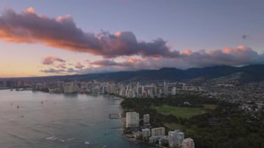 Altın gün batımında Kapiolani Bölge Parkı. Waikiki tatil köyleri ile şehir merkezindeki modern şehrin hava manzarası. Oahu adasındaki Honolulu şehrinin üzerinde güzel bir yaz günbatımı. Hawaii adası manzarası 4K