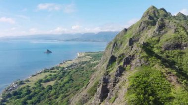 Dramatik dağların, mavi okyanusun, Hawaii Oahu adasının nefes kesici manzarası. Kualoa Çiftlik Vadisi Panoraması 'ndaki tropik plajlı yüksek yeşil orman zirveleri boyunca uçan güzel doğa dronu.