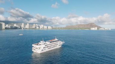 Oahu adasındaki Waikiki kıyısında gün batımı gezisi. Hawaii turizm geçmişi. Gezi teknesinde turistik eğlence ve yemek ve yalvarma şovu. Beyaz gemi Honolulu ve Diamond baş görüntüleriyle hareket ediyor.
