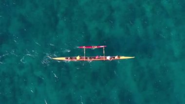 Oahu 'da geleneksel Hawaii kanosuyla gezen atletizm insanlarına tepeden bakıyorduk. Açık mavi okyanus sularında su aktivitesi 4K. Spor takımının yukarıdan aşağı kanoyla açıldığı bir sahne.