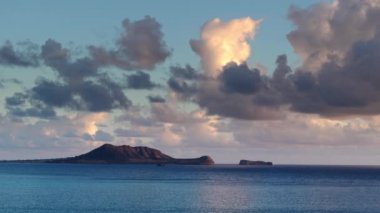 Oahu adasının rüzgarlı kıyılarında kaplumbağa şeklinde bir ada. Güzel kaplumbağa adasının hava manzarası sabahın erken saatlerinde mavi okyanusun üzerinde süzülen beyaz kabarık bulutlarla birlikte. Gün doğumunda 4K