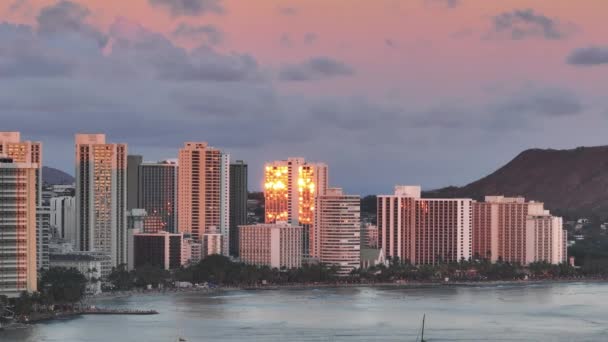 近代的な海洋フロントホテルで輝く美しい黄金の太陽 風光明媚なオアフ島のダイヤモンドヘッドの上に風光明媚なピンクライラック雲 ハワイ旅行先 アメリカ ワイキキリゾートエリアのシネマティックサンセット — ストック動画
