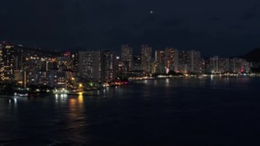 Waikiki sahilindeki tatil köylerinde. Geceleri aydınlatılmış güzel Honolulu modern binaları. Hava karardıktan sonra Hawaii 'nin en büyük şehrinden insansız hava aracı vuruldu. Şehir merkezindeki tropik ada Oahu 4K turizmi