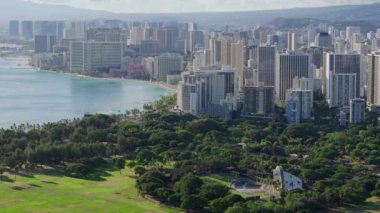 Oahu adasındaki Honolulu şehrinde güneşli güzel bir yaz günü. Şehir merkezindeki Waikiki tatil köyünün hava manzarası. Altın gün ışığında Kapiolani Bölge Parkı. Hawaii adası manzarası 4K