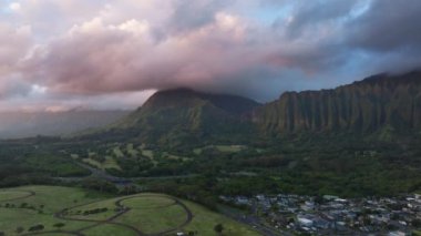 Honolulu Watershed Ormanı 'nı kaplayan yağmur bulutlarındaki ilk güneş ışınları. Dik orman tropikal dağı. Oahu adasındaki Kaneohe kasabasının havadan görünüşü. Pembe gündoğumunda manzaralı dağ sırtı