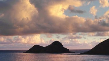 Na Mokulua adalarının siluetleri parlak bulutların altında okyanusta. Hawaii adalarında manzaranın dramatik arka planı. Güneş doğarken rüzgârlı kıyılarda iki küçük ada ile Oahu turizmi kavramı