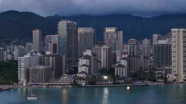 Altın gün batımı ışığı modern cam binalara yansıyor. Honolulu, Oahu Hawaii 'deki hava üssü. Limana bakan Waikiki tatil köyündeki gül rengi gökyüzü yansıması. Dağın arka planında dramatik bulutlar.