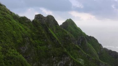 Yeşil orman dağları ve Jura dönemi sahnesi. Kasvetli yağmurlu bir günde dramatik doğa manzarası. Jurassic volkan doğalı Kualoa parkı. Dik tropik dağ sırtı olan Hawaii adası kıyı şeridi.