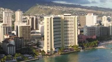 Altın gün batımında Waikiki plaj tatil beldelerinde panoramik manzara. Honolulu 'nun ünlü Waikiki plajındaki modern otel binaları. Oahu Adası turizm geçmişi. Hawaii adalarındaki havacılık şehri manzarası 4K US