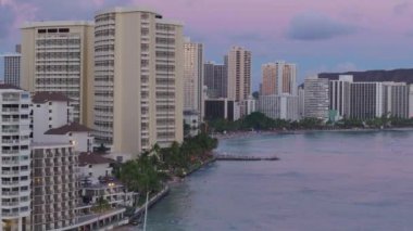 Hawaii seyahat hedefi ABD. Waikiki yaz tatili otellerinde gün batımı sineması. Modern okyanus manzaralı otellerde parlayan güzel altın güneş 4K. Oahu Adası 'ndaki Waikiki otellerinin üzerinde pastel gökyüzü