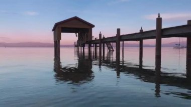 Doğa arkaplan gökyüzü suya yansıyor. Alacakaranlıkta ayna gölünün yukarısındaki ahşap kayıkhanenin huzurlu arka planı. Geriye doğru uçarak mavi Tahoe gölünün üzerinde ufukta dağlarla birlikte tersten uçuyor.