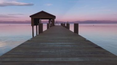 Doğa arkaplan gökyüzü suya yansıyor. Alacakaranlıkta ayna gölünün yukarısındaki ahşap kayıkhanenin huzurlu arka planı. Geriye doğru uçarak mavi Tahoe gölünün üzerinde ufukta dağlarla birlikte tersten uçuyor.