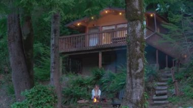 Genç bir kadın, sık dağ ormanlarında gizlenmiş, açık havada, ahşap bir kulübede oturuyor. Doğa tefekkür kavramı. Hafta sonu gezisi, güzel doğa 4K USA 'de dinlenmek ve ferahlamak için.