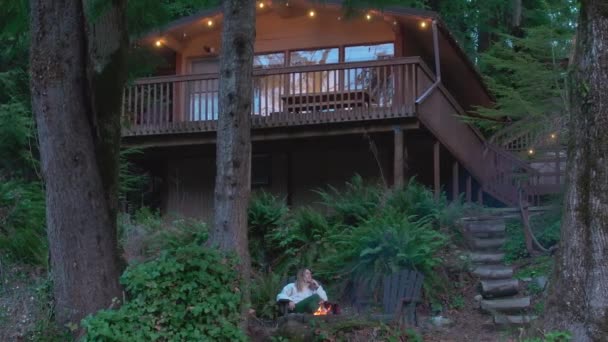 大自然的概念在沉思 周末旅行 在美丽的自然4K美国 放松一下户外和休息一下 年轻女子坐在茂密的山林中的火坑外舒适的木屋里 视频剪辑
