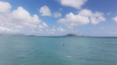 Bir insan, Oahu, Hawaii, ABD açıklarındaki engin okyanus sularında sörf yapıyor. Bireyler ustalıkla dalgalarda geziniyor ve açık suların tadını çıkarıyor..