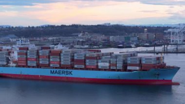 Seattle, Washington, ABD - 28 Aralık 2023: Seattle limanına yanaşmış renkli konteynırlarla dolu bir Maersk kargo gemisi, günbatımında arka planda vinç ve stadyum bulunuyor..