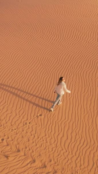 バーティカルビデオ 砂漠の広大な広がりの中に立っている人は 澄んだ青空の下に無限の砂丘に囲まれています — ストック動画