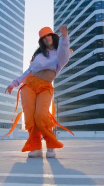 Dikey video. Düşük açılı sinematik çekim dansçısı genç yetenekli sokak dansçısı şehirde serbest stil hip hop hareketleri yapıyor. Modern danstan hoşlanan karışık yarış modelleri. Moda yaşam tarzı