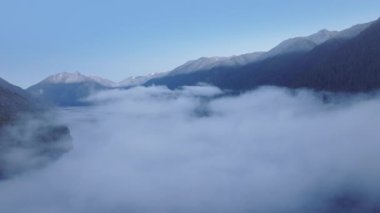 Havadan insansız hava aracı yoğun sis bulutunu yakalıyor tepelerinde dağ zirveleri olan sakin bir gölü örtüyor. Dinginlik, sabahın erken saatlerinde sakinliğe hitap eder. 4K görüntü. 