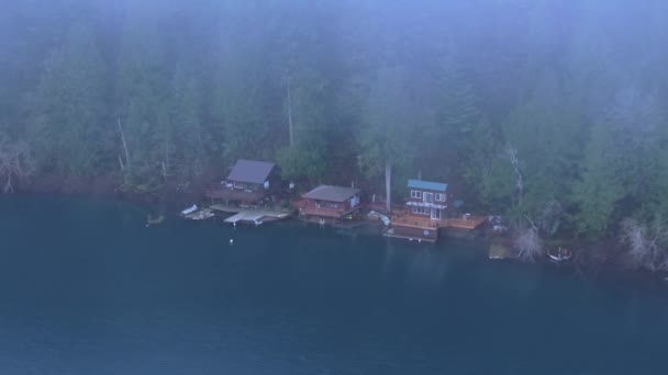 ワシントン州の密集した常緑樹林に囲まれた穏やかな湖の端に囲まれた密閉された小屋の空中観察は 自然の環境で平和的な後退を示しています 4K映像について — ストック動画