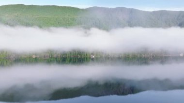 Bu dingin hava manzarası, Washington 'daki canlı yeşil dağlarla çevrili yansıtıcı bir gölün üzerinde süzülen bir sabah sisi tabakasını gösteriyor. 4K görüntü. 