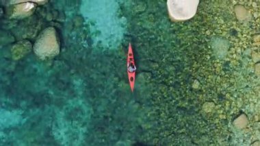 Suyun üzerinde kırmızı bir kano içinde yeşil çalılarla çevrili bir insanın kuş bakışı görüntüsü. Su altı bitkileri temiz sulara bakar.