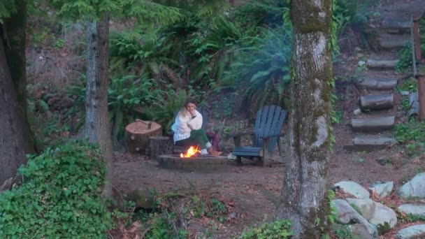 Woman Sitting Fire Pit Woods Wooden House River Surrounded Trees — Vídeos de Stock