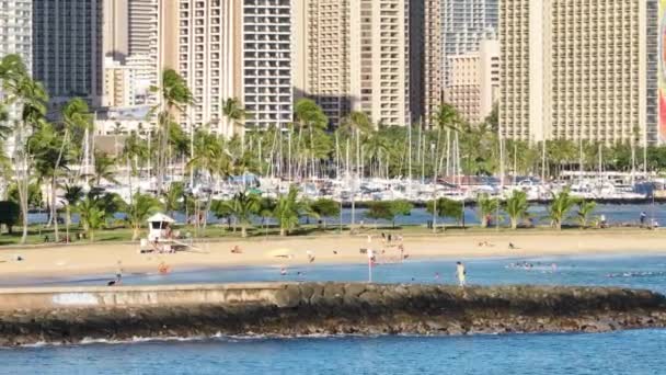 美国夏威夷瓦胡岛 2023年8月11日 视频展示了一个面对繁忙城市的沙滩 当人们在阳光明媚的天空下享受各种海滩活动时 海浪轻轻地冲击着海岸 — 图库视频影像