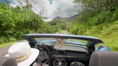 Neşeli bir kadın, Oahu 'daki bir parkta serin bir yolculukta esen meltemi hisseder üstü açık arabası, yemyeşil Hawaii manzaralarının önünden süzülür. 4K görüntü. 