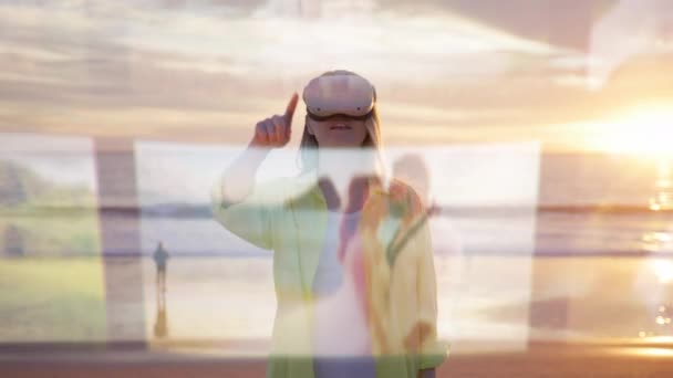 黄色いシャツを着た若い女性はVrヘッドセットを着て 仮想ジェスチャーでデジタル写真をスワイプし 夕日のビーチの素晴らしい背景に立ち向かいます 4K映像について — ストック動画
