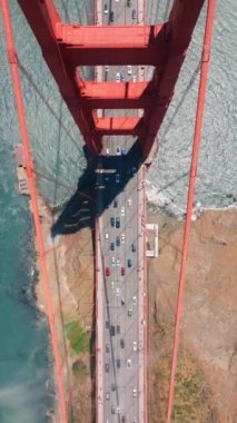 Dikey Ekran: Doğrudan Golden Gate Köprüsü 'nün üzerinde trafik ve körfezin turkuaz sularını aydınlatan bir hava perspektifi. 