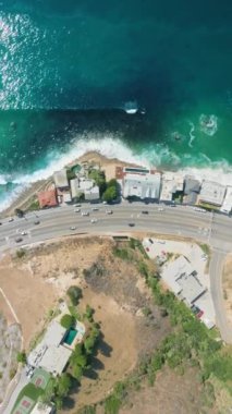 Dikey Ekran: Malibu 'da Crisp Blue Ocean, Showcasing Urban ve Natural Beauty' nin yanında koşan bir sahil caddesinin büyüleyici hava görüntüsü. 4K Görüntü. 