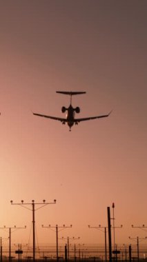 Dikey ekran: Güneş batarken, bir uçak zarif bir şekilde havaalanına iniyor, ticari havacılık için güvenli bir anı simgeliyor. Sahne, sektörde güvenliğin önemini vurguluyor.