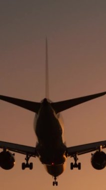 Günbatımında inen bir uçağın dikey görüntüsü alacakaranlık gökyüzüne karşı uçağın siluetini gösteriyor. Sahne, bir uçağın gelişinin güzelliğini ve huzurunu yakalar.