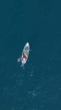 Dikey ekran: Büyüleyici bir dikey video, yukarıdan bir dron 'un sakin, berrak mavi sularda zarafetle süzülen bir tekneyi görüntülemesini gösteriyor. Dikey format, barışçıl deniz görünümüne ekleniyor